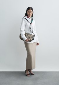 Biała koszula z długim rękawem i czarnym szalikiem, beżowa spódnica, czarne sandały na ramiączkach oraz torebka na ramię w kropki.