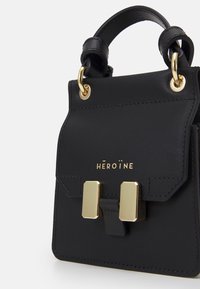 Sac à main en cuir noir avec quincaillerie dorée, doté d'une fermeture à rabat et d'une boucle proéminente. Texture lisse avec des détails de couture subtils.