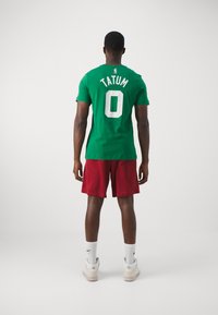 Grøn basketballtrøje med hvid tekst "TATUM" og nummer "0" på ryggen. Matchet med røde shorts, hvide sportssokker og lyse sneakers.