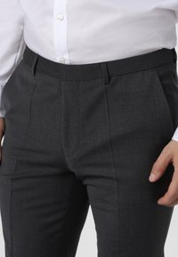 Gray tailored trousers with a smooth texture, featuring double pleats and side pockets, paired with a white button-up shirt.