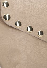 Beige leren clutch met een gestructureerd oppervlak, versierd met metallic gouden studs langs de rand.
