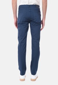 Pantaloni slim-fit blu navy realizzati in cotone con una texture liscia, dotati di tasche posteriori e dettagli di cucitura sottili. Sneakers bianche sotto.