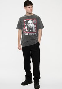 Gray cotton t-shirt featuring a graphic print of a face, bordered in red. Paired with black pants and black lace-up boots.