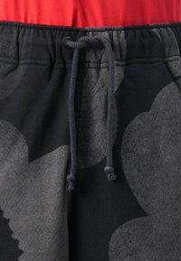Pantaloni della tuta neri con un grande motivo floreale grigio, vita elasticizzata con una rifinitura rossa e un cordino con perline grigie.