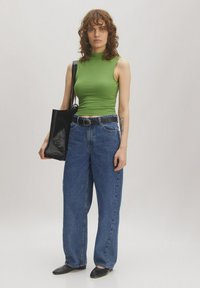 Groene ribbelige top met hoge hals, brede blauwe denim jeans, zwarte tote tas en zwarte schoenen met puntige neuzen. Gladde stof en relaxte pasvorm.