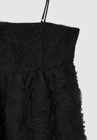 Schwarzes Kleid mit dünnen Trägern, das mit geschichteten Stoffrosen über dem Oberteil und dem Rockbereich verziert ist und ein strukturiertes florales Muster erzeugt.