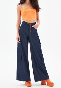 Oranje crop top met gestructureerd ontwerp, gecombineerd met donkerblauwe wijde cargobroek met twee zijzakken en een touwtje in de taille.