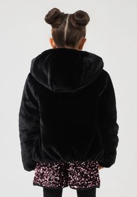 Giacca nera in plush con cappuccio e una consistenza morbida, abbinata a una gonna di paillettes rosa lucida. La giacca presenta una vestibilità ampia e polsini elasticizzati.