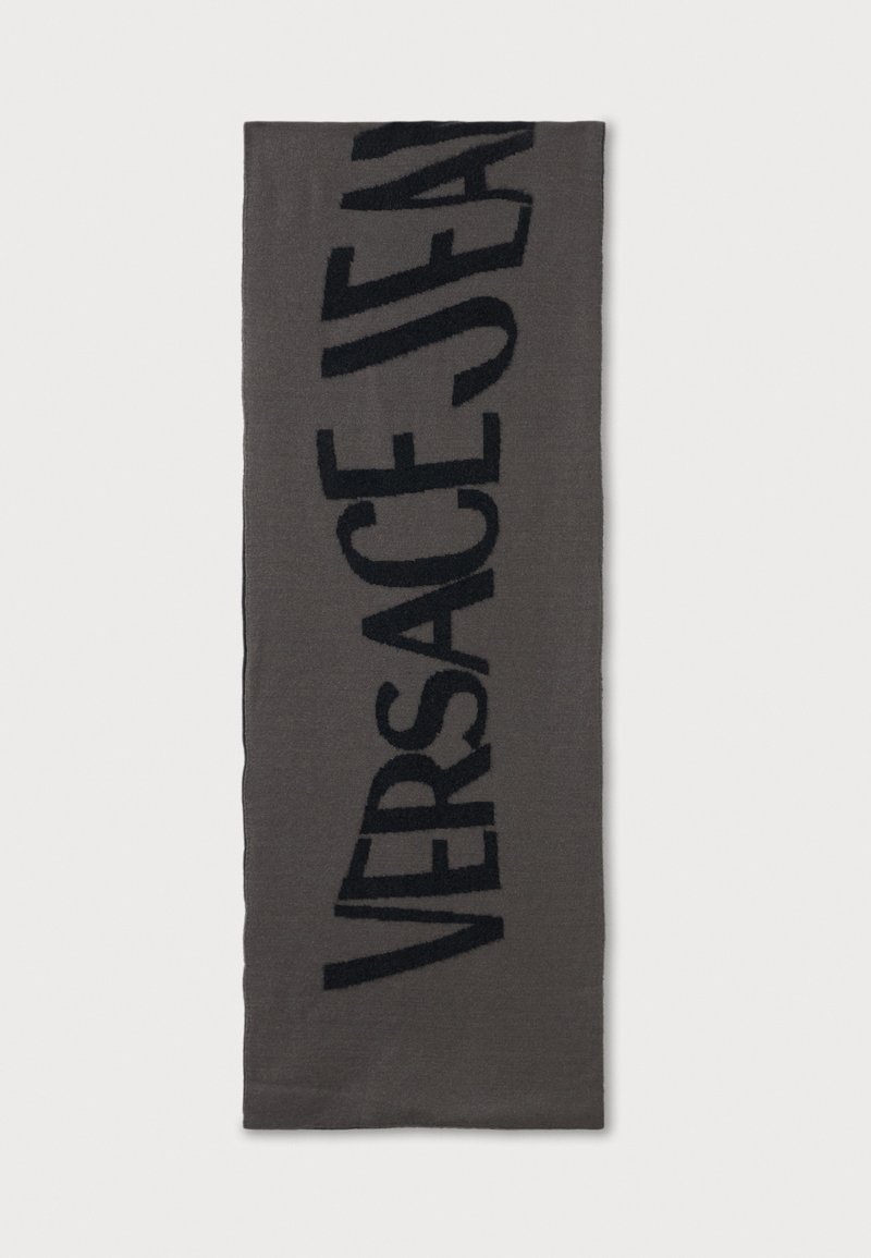 Sivi šal s mekom teksturom, s istaknutim crnim logoom "VERSACE JEANS" u debelim slovima. Pravokutnog oblika, minimalističkog dizajna.