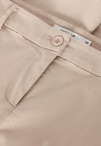Beżowe spodnie o gładkiej fakturze, z zapięciem na guzik i metką na pasku z rozmiarem 38.