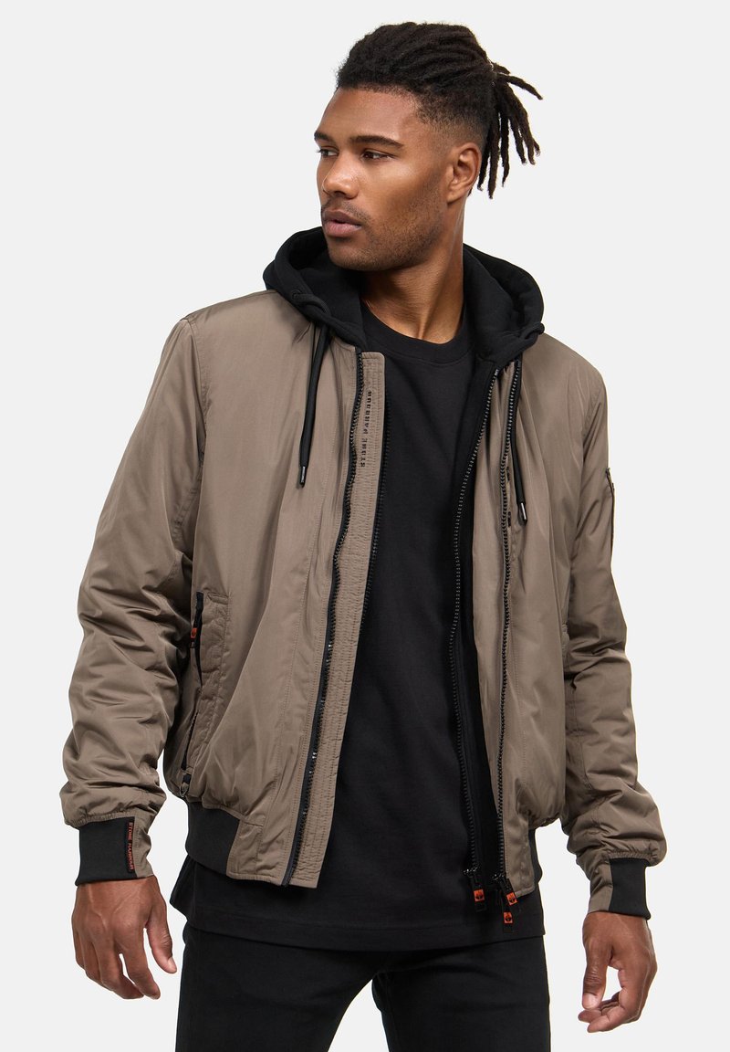 Giacca bomber in un tan smorzato, con design con cappuccio, zip frontale, polsini elasticizzati e tasche laterali con dettagli in hardware a contrasto.