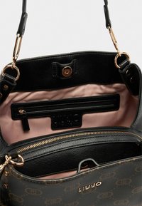 Borsa a mano in pelle nera con interno rosa chiaro, dotata di una tasca con zip, etichetta del logo e accessori in ottone dorato. La texture è liscia con un design strutturato.