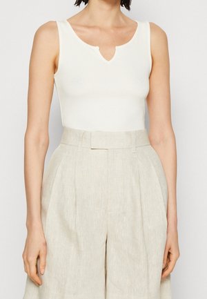 Hvid ærmeløs top med V-hals, lavet af glat stof, parret med lysebeige, højtaljede, plisserede linnedshorts.