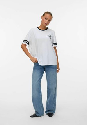 T-shirt en coton blanc avec des rayures noires sur les manches et le texte "PARIS 1975". Associé à un jean léger bleu clair à taille haute et coupe ample.