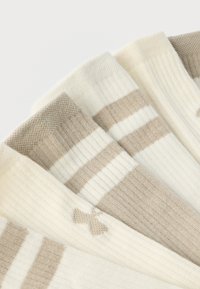 Μαλακές πλεκτές κάλτσες σε αποχρώσεις απαλού μπεζ και λευκού με ρίγες, τοποθετημένες σε σχήμα βεντάλιας σε λευκό φόντο, τονίζοντας την ριμπ υφή και τα διακριτικά σχέδια.