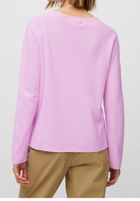 Suéter rosa texturizado de manga larga con escote en la espalda, combinado con pantalones de tono beige claro. La tela tiene una apariencia suave y de tejido de punto.