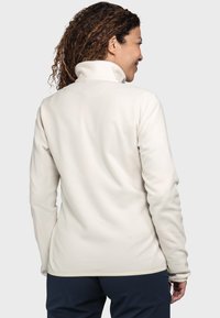 Helle Fleecejacke mit hohem Kragen, langen Ärmeln und weicher Textur. Merkmale sind eine glatte Oberfläche und eine taillierte Silhouette.