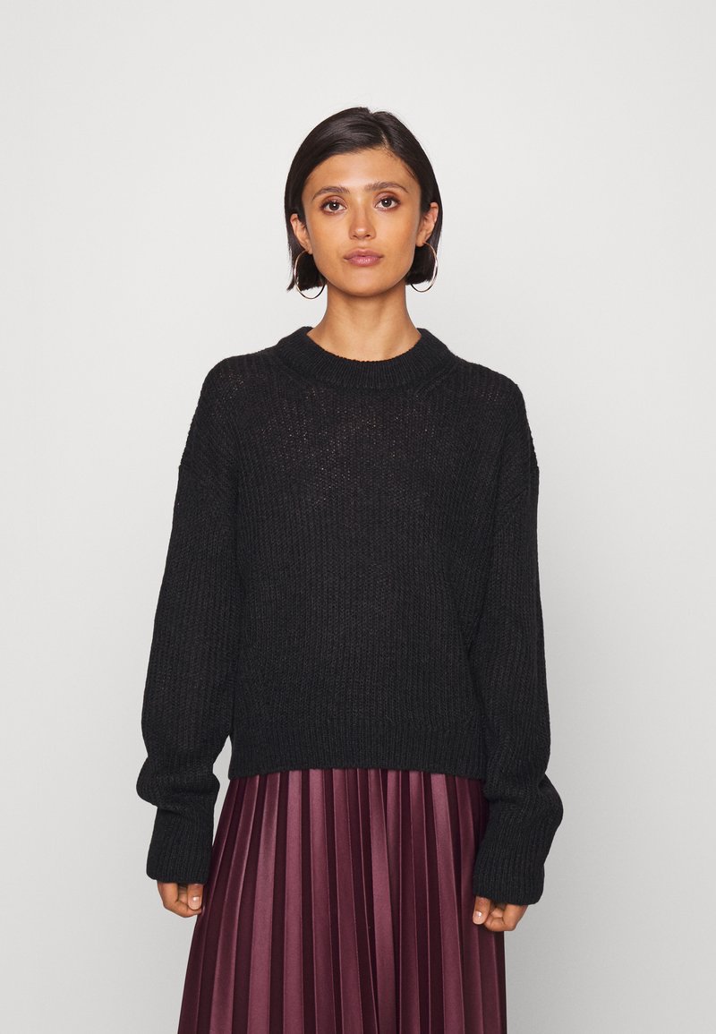 Schwarzer Strickpullover mit geripptem Muster, lässig fallenden Schultern und Rundhalsausschnitt, kombiniert mit einem burgunderrot plissierten Rock.