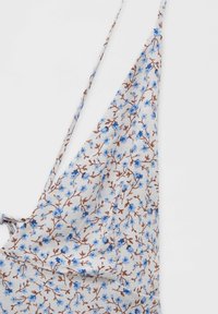 Tissu blanc avec fines bretelles et petit imprimé floral bleu entrelacé de branches brunes.