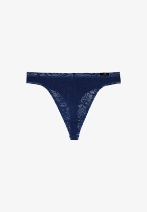 Marineblauwe kanten string met bloemenpatroon, elastische tailleband en een label aan de achterkant. Dunne bandjes en een doorschijnende textuur versterken het ontwerp.