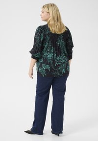 Blusa nera a fiori con motivi verdi, maniche a campana a tre quarti, smocking elastico sul retro, abbinata a jeans blu a gamba dritta e scarpe nere con punta.