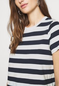Pruhované tričko z jersy s námořnickými modrými a bílými vodorovnými pruhy, kulatým výstřihem a krátkými rukávy, v uvolněném střihu a s jemnou strukturou.