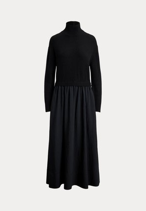 Robe longue noire avec un haut à col roulé ajusté, des manches longues et une jupe plissée fluide, sur un fond uni.