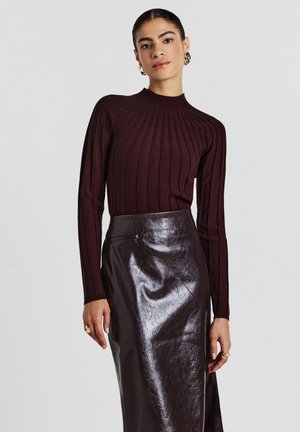 Burgunderfarbene gerippte Stricklongsleeve mit hohem Kragen, kombiniert mit einem glänzenden schwarzen Bleistiftrock aus Kunstleder mit glatter Textur.