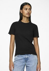 Svart ribbet t-skjorte med kort erme, med bølgete mansjetter og rå nederkant, sammen med lyseblå denimjeans.