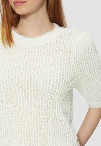Biały sweter z teksturowanej dzianiny z okrągłym dekoltem i krótkimi rękawami, o luźnym kroju i widocznym pionowym szwem.