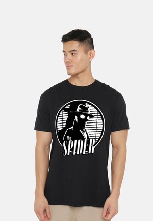 Man wearing black t-shirt with white graphic of a mysterious figure in hat and glasses with text "The Spider" on front.
