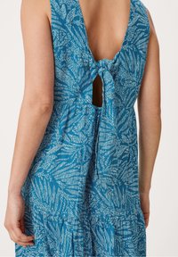 Robe bleue à motifs avec un nœud au dos, un col rond et un tissu texturé aux motifs évoquant des feuilles.