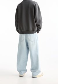 Ciemnoszara, oversize'owa bluza zestawiona z jasnoniebieskimi, luźnymi dżinsami, charakteryzującymi się gładką fakturą i swobodnym krojem. Minimalistyczny design.