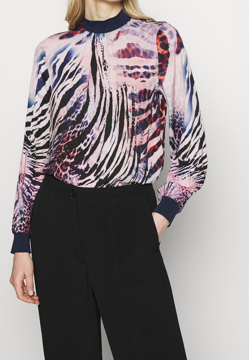 Long-sleeve blouse in multicolored animal print with a high neckline and navy cuffs. Worn with black tailored pants. Smooth, lightweight fabric.