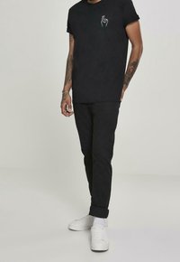 Zwarte katoenen T-shirt met een witte handafbeelding op de borst, gecombineerd met zwarte jeans en witte sneakers. Eenvoudig, modern ontwerp.
