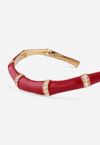 Fascia per capelli rossa in plastica con finitura lucida. Presenta dettagli in oro e strass trasparenti, modellata a segmenti di bambù.