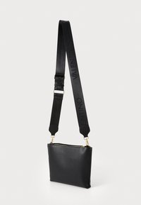 Sac bandoulière en cuir noir avec une finition texturée, équipé d'une fermeture éclair dorée et d'une bandoulière réglable avec un marquage en relief.