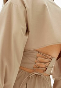 Beige topp med en kortad design som har puffärmar och ett spetsat baksidesdetalj. Mjukt tyg och en slät textur är påtagliga.