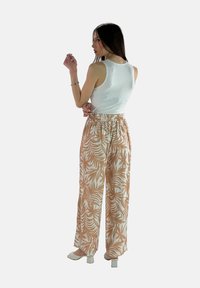 Witte tanktop en lichtbeige broeken met een patroon van palmbladeren. De broeken hebben een elastische tailleband, een relaxte fit en wijde pijpen.
