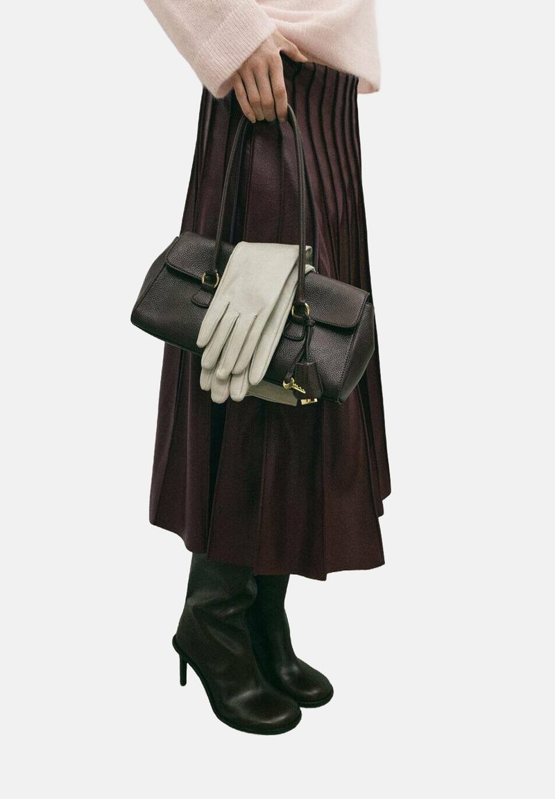 Bolso de cuero marrón con detalles dorados, guantes grises, falda plisada marrón oscuro y botas negras de tacón hasta la rodilla. Se aprecian materiales de textura suave.