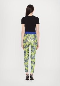 Top negro ajustado de manga corta combinado con leggings verdes ceñidos con lentejuelas que tienen una cinturilla de patrón azul. Sandalias negras de tacón alto.