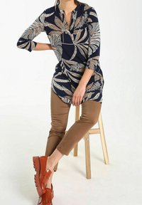 Granatowy tunik z złotym i białym wzorem kwiatowym, w połączeniu z beżowymi spodniami i brązowymi butami. Zawiera rękawy 3/4 i okrągły dekolt.
