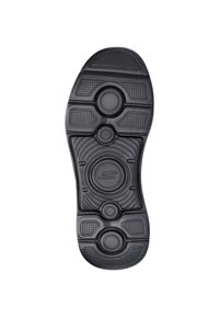 Zwarte rubberen schoenzool met gestructureerde patronen, ronde accenten en een glad centraal logo. Ontwerp met antislip grip zichtbaar.
