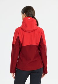 Red waterproof jacket with a hood, featuring a color-block design in dark and bright red shades. Smooth texture with a fitted cut.