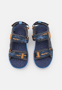 Niebiesko-pomarańczowe sandały w wzory z podwójnymi regulowanymi paskami, teksturowaną wkładką i białą podeszwą. Przywodzą na myśl sportowy design.