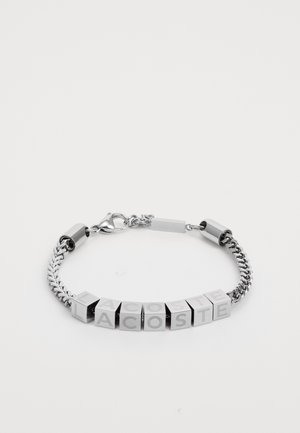 Bracciale in argento con design a catena e maglie cubiche che formano la scritta "LACOSTE". Superficie metallica liscia, finitura brillante e chiusura a moschettone.