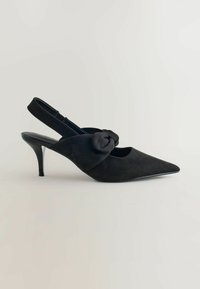 Schwarze Wildleder Slingback-Pumps mit niedrigem Stiletto-Absatz, spitzem Zehenbereich und dekorativem Knotendetail auf der Oberseite.