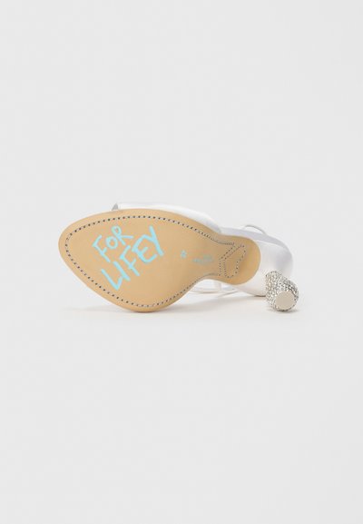 Scarpa con tacco bianca con un accento di glitter metallico, che mostra una suola beige con il testo "FOR LIFETY" in blu. Materiale liscio, design elegante.