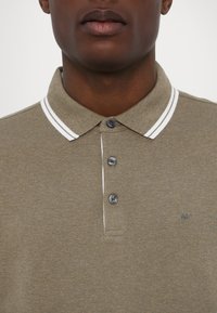 Olivengrønn polo skjorte med tre-knappers lukking, kontrasterende hvite striper på kragen, og brodert "MK" logo på brystet.