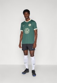 Zöld focimez kerek nyakkal és krémszínű díszítéssel, középen logóval. Fekete nadrággal és fehér zoknival viselve.